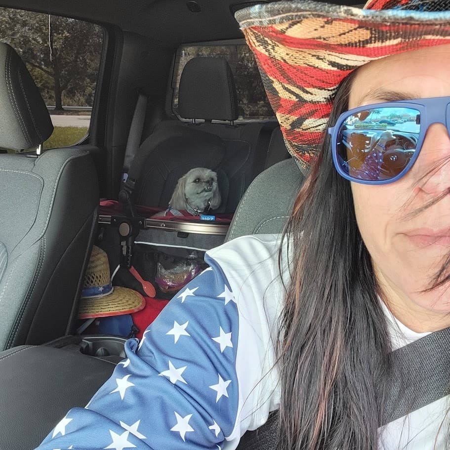 Momma in a flag sleeve and blue sunglasses with Paris riding in her carrier in the back seat on the Fourth of July.