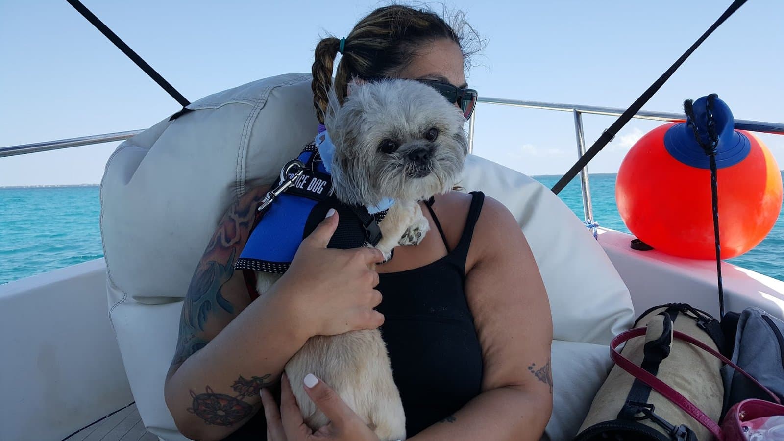 Paris in her blue harness held in The Other Momma's arms on the boat, turquoise water and a red buoy behind them