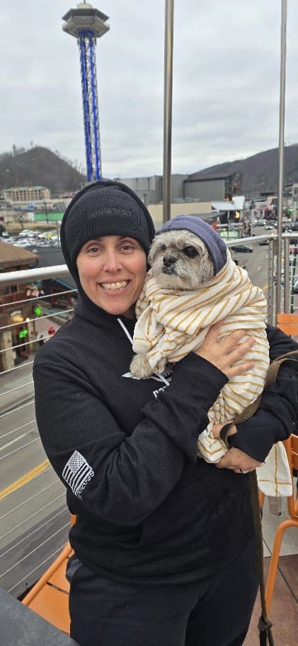 Momma in a beanie holding Paris, wrapped in a striped blanket, a tall tower ride behind them in Gatlinburg