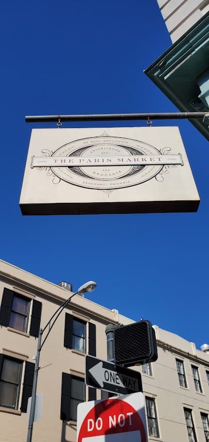 A hanging sign reading The Paris Market against a bright blue Savannah sky
